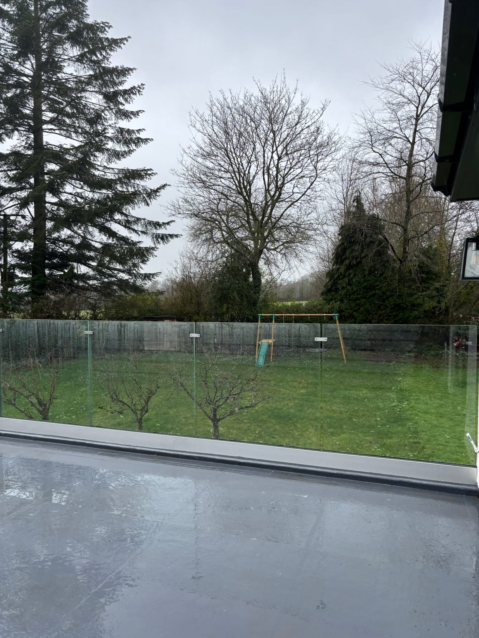 View from balcony through frameless glass balustrade panels over large garden in Doncaster