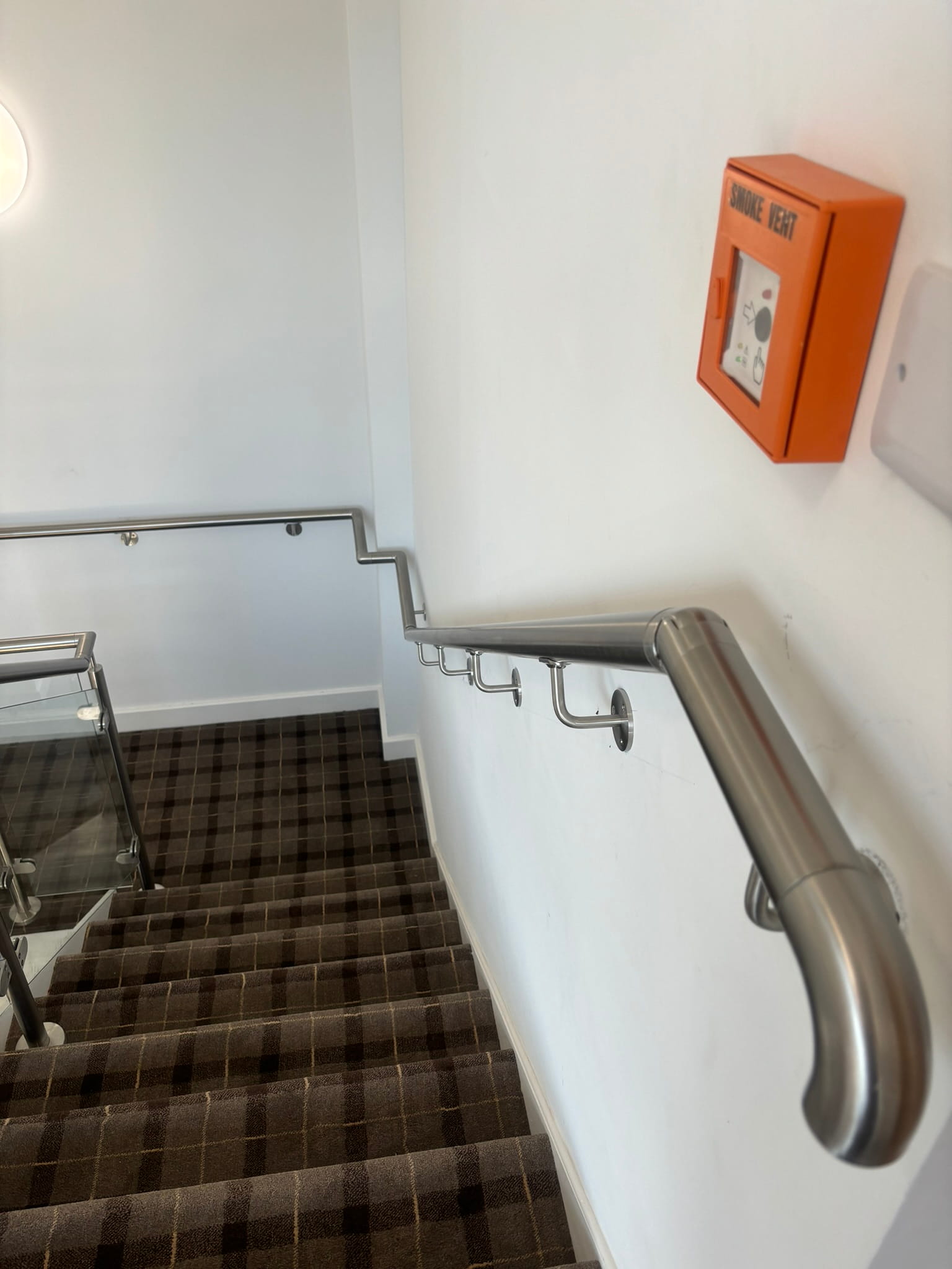 Brushed stainless steel wall-mounted handrail on HMO staircase in Rotherham beside glass balustrade