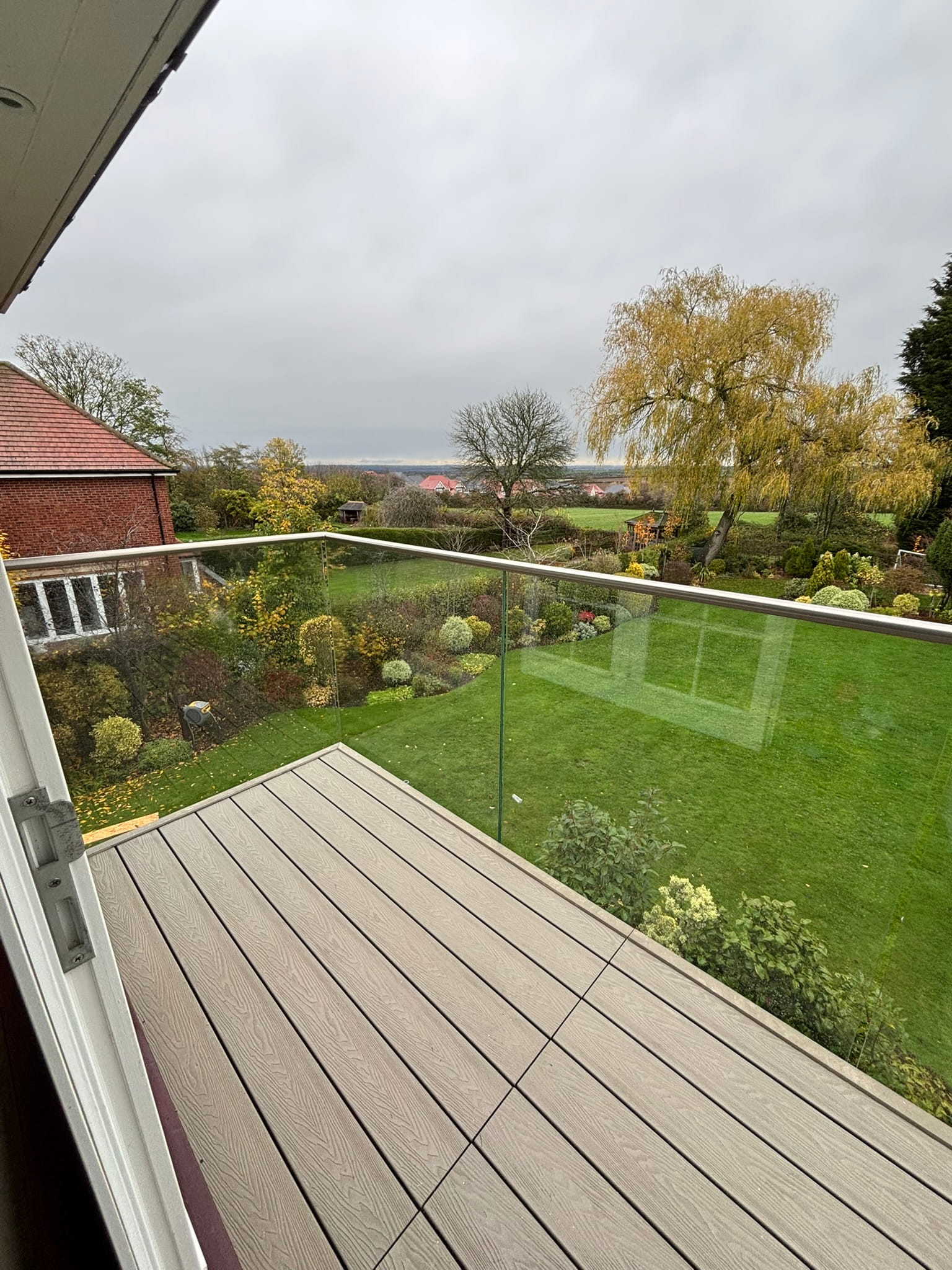 Renovated frameless glass balustrade with stainless steel handrail and composite decking on residential balcony, Nottingham