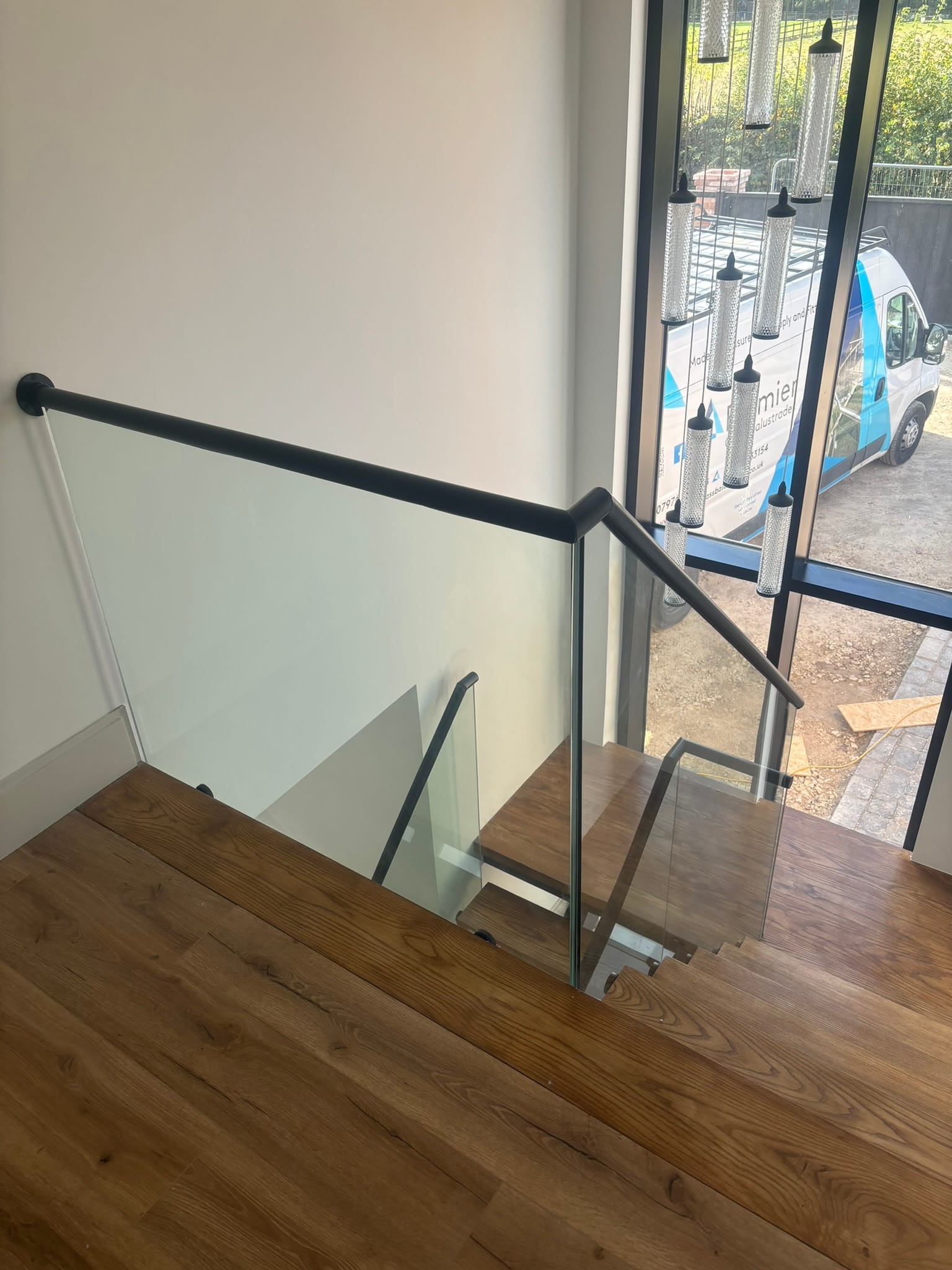 Black continuous handrail on frameless glass balustrade alongside oak staircase