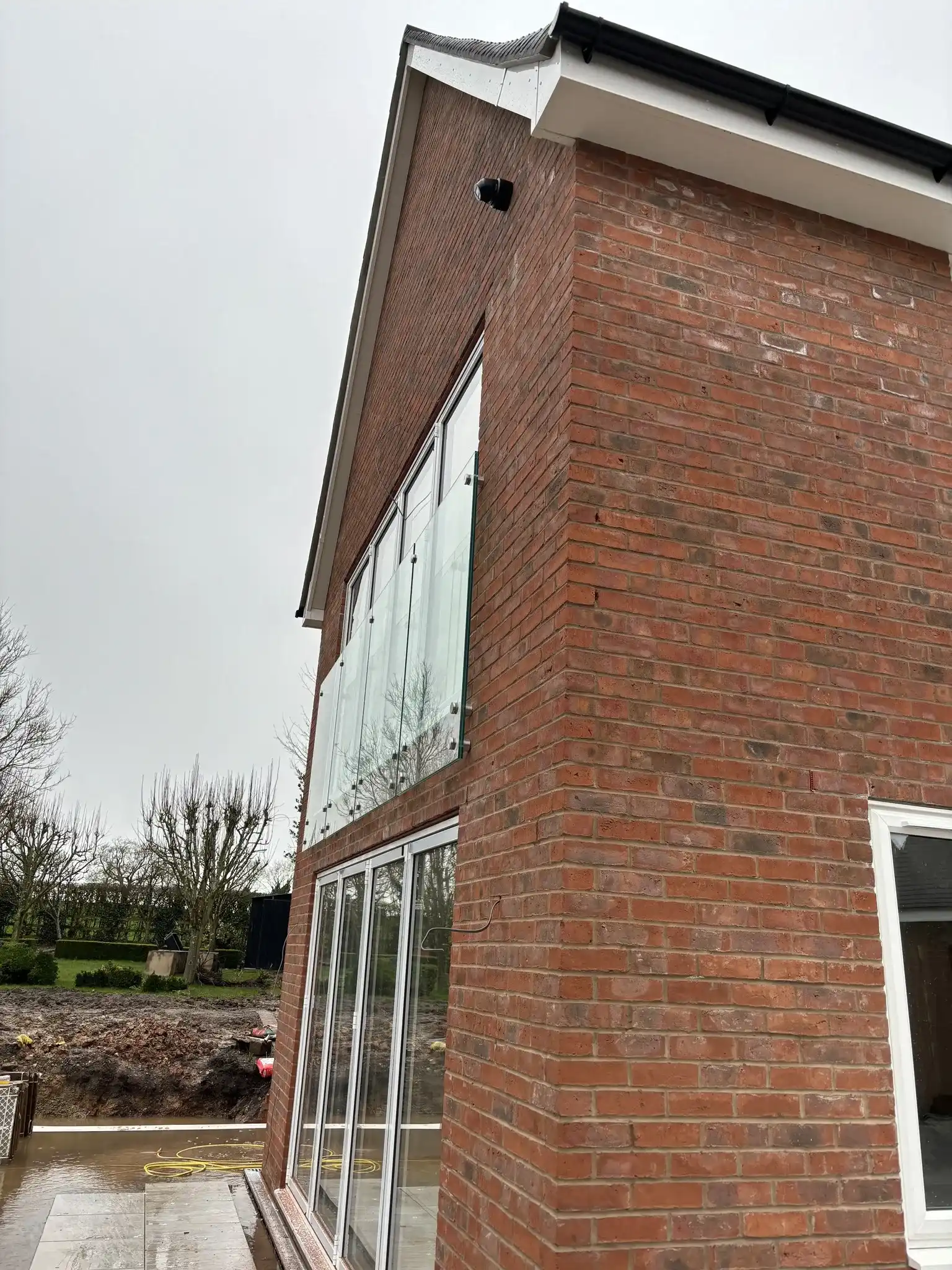 Corner view of frameless juliet balcony panels face-fixed to brickwork on Chesterfield new build