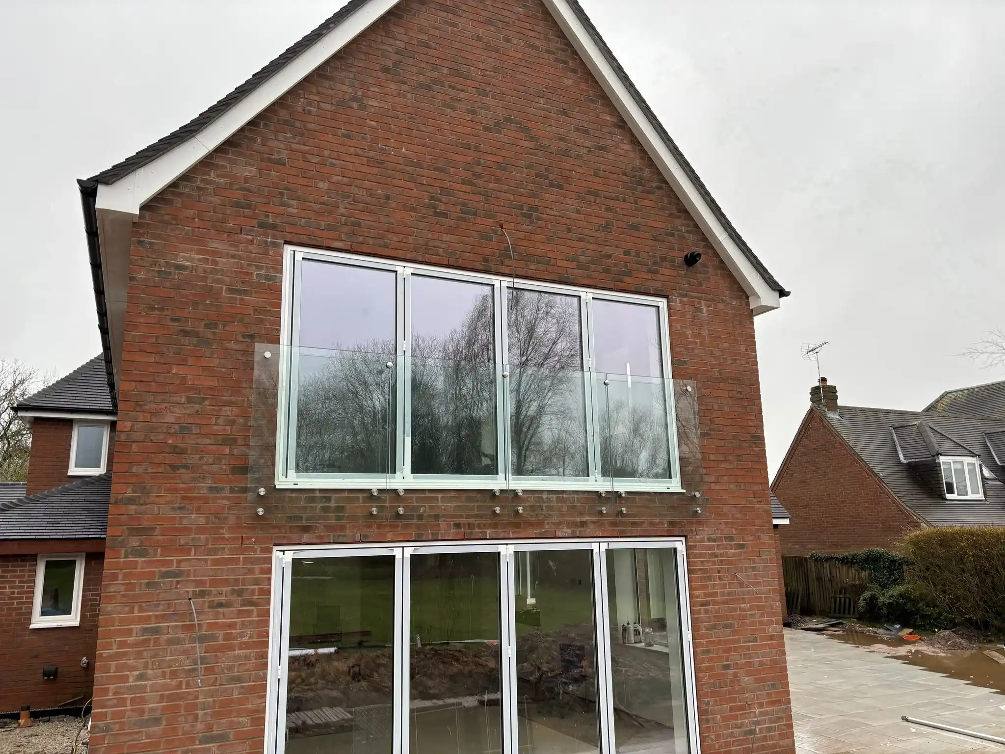Rear view of new-build Chesterfield home with frameless glass Juliet balcony above bifold doors.
